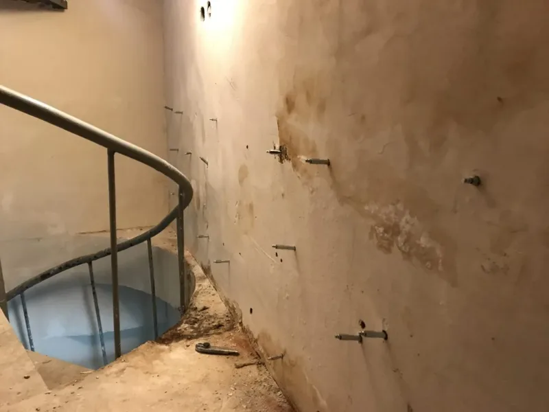 Zawilgocona ściana z pakerami przy kręconych schodach prowadzących w dół